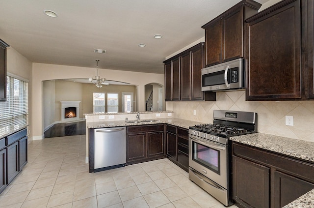 kitchen with sink, decorative backsplash, kitchen peninsula, stainless steel appliances, and light stone countertops