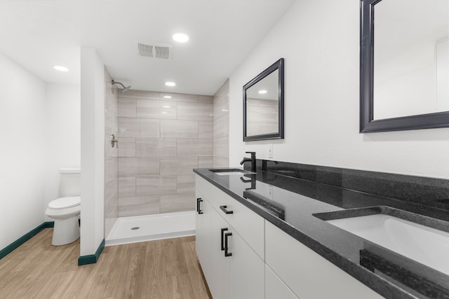 bathroom featuring hardwood / wood-style flooring, tiled shower, vanity, and toilet