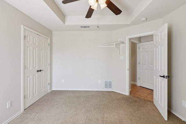 unfurnished bedroom featuring light carpet, ceiling fan, a closet, and a raised ceiling