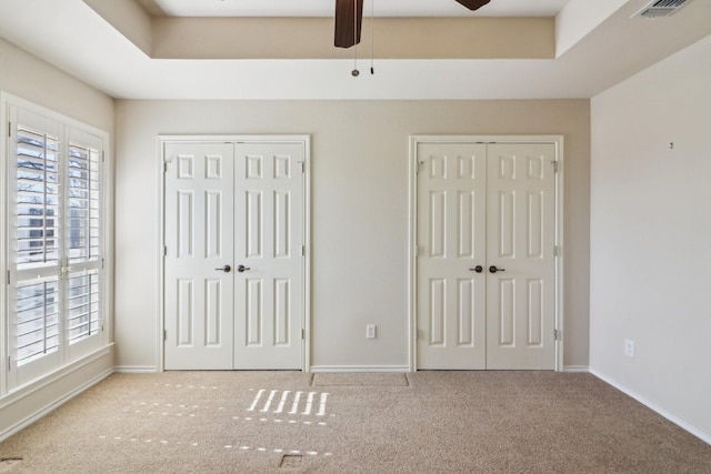 unfurnished bedroom featuring ceiling fan, multiple windows, carpet, and multiple closets