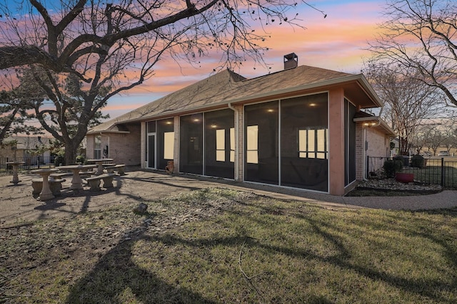 back house at dusk featuring a sunroom and a lawn