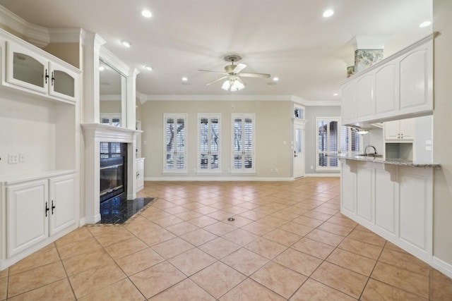 unfurnished living room featuring a high end fireplace, light tile patterned floors, crown molding, and ceiling fan