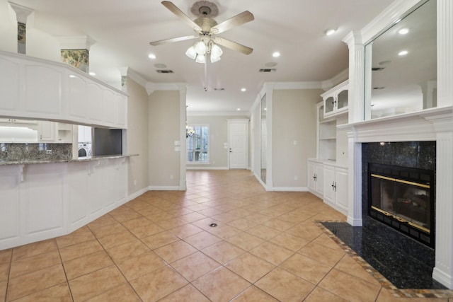 unfurnished living room with ceiling fan with notable chandelier, a high end fireplace, light tile patterned flooring, and crown molding