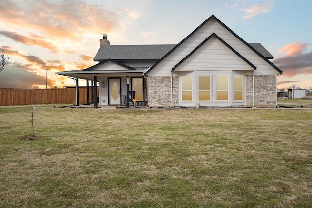 back of house at dusk with a yard, fence, a chimney, and brick siding