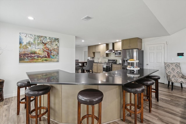 kitchen featuring light hardwood / wood-style floors, a breakfast bar area, stainless steel appliances, backsplash, and wall chimney exhaust hood