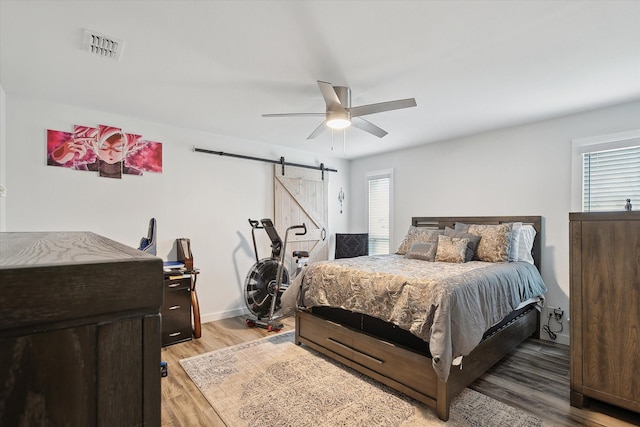 bedroom with ceiling fan, a barn door, and wood-type flooring