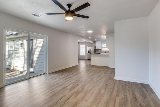 unfurnished living room with a textured ceiling, ceiling fan, and light hardwood / wood-style floors