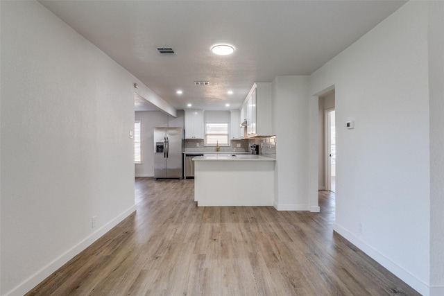 kitchen with kitchen peninsula, decorative backsplash, light hardwood / wood-style flooring, stainless steel appliances, and white cabinets