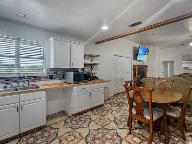 kitchen featuring ceiling fan, tasteful backsplash, crown molding, white cabinets, and sink