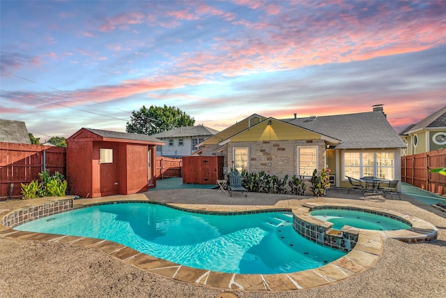 pool at dusk with a storage unit, a patio area, and an in ground hot tub