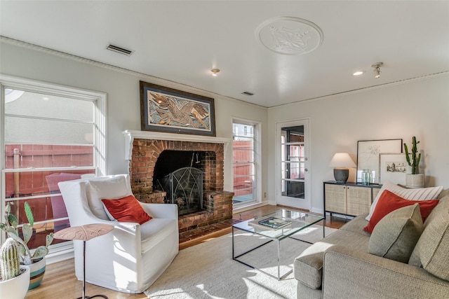 living room with a brick fireplace, light hardwood / wood-style floors, and crown molding