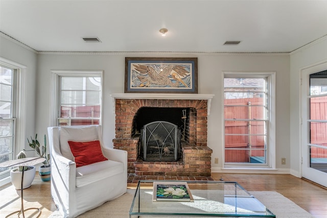 living room with a brick fireplace, crown molding, and light hardwood / wood-style floors