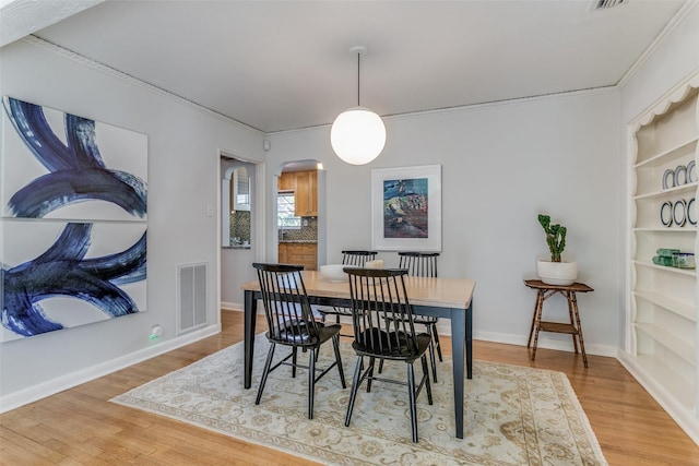 dining space featuring built in shelves, crown molding, and light wood-type flooring