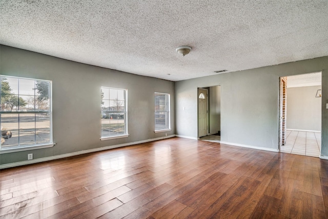 unfurnished room with a textured ceiling, a healthy amount of sunlight, and wood-type flooring