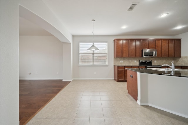 kitchen featuring pendant lighting, stainless steel appliances, sink, backsplash, and light tile patterned floors