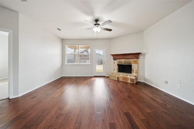 unfurnished living room with ceiling fan, dark hardwood / wood-style flooring, and a stone fireplace