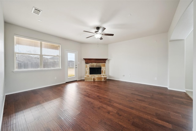 unfurnished living room featuring ceiling fan, dark hardwood / wood-style floors, and a stone fireplace