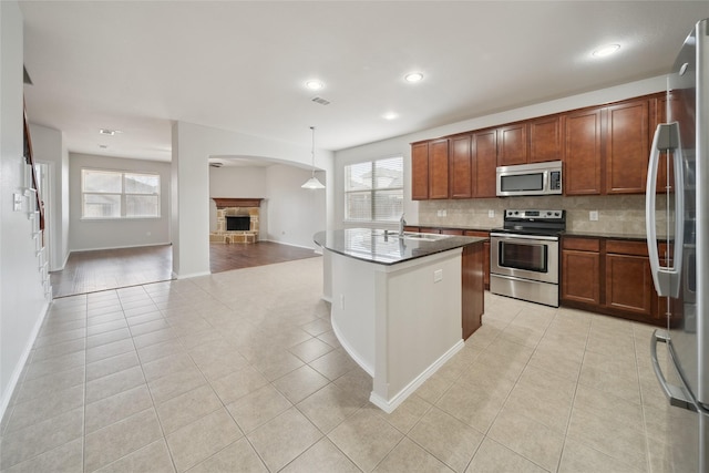 kitchen featuring a stone fireplace, appliances with stainless steel finishes, decorative light fixtures, light tile patterned flooring, and sink