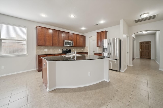 kitchen with backsplash, a center island with sink, sink, appliances with stainless steel finishes, and light tile patterned floors