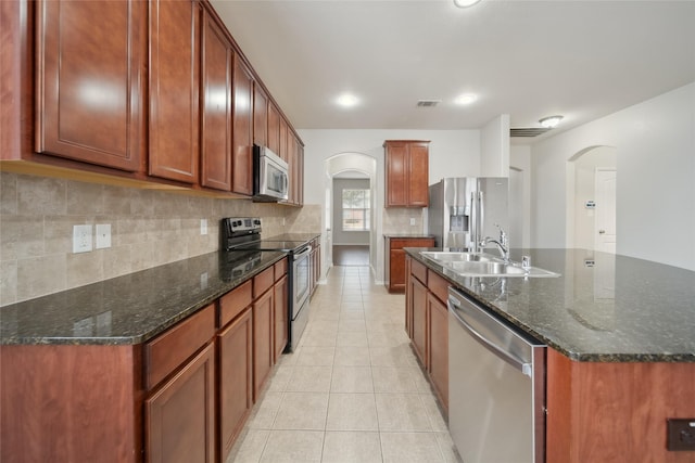 kitchen with light tile patterned floors, stainless steel appliances, decorative backsplash, dark stone countertops, and sink