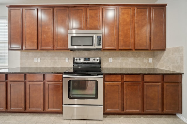 kitchen with backsplash, light tile patterned floors, stainless steel appliances, and dark stone countertops