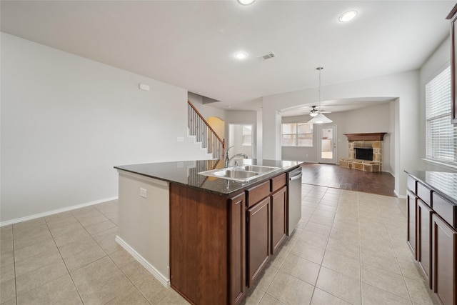 kitchen featuring ceiling fan, a kitchen island with sink, light tile patterned flooring, a fireplace, and sink