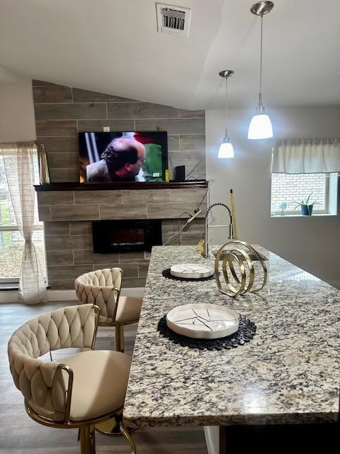 kitchen featuring hanging light fixtures, vaulted ceiling, light stone countertops, and a tile fireplace