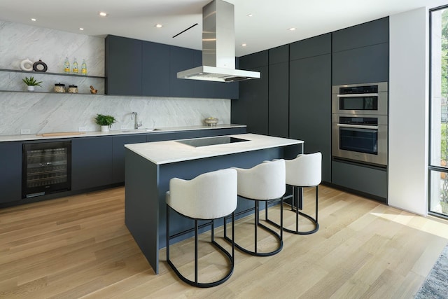 kitchen with stainless steel double oven, a center island, a kitchen bar, wine cooler, and island range hood