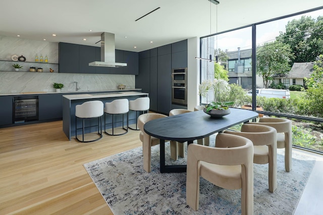 dining space featuring floor to ceiling windows, bar area, light hardwood / wood-style flooring, and wine cooler