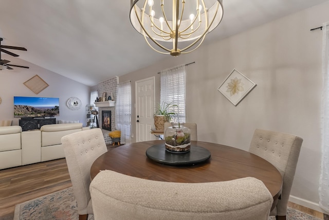 dining space featuring hardwood / wood-style flooring, ceiling fan with notable chandelier, lofted ceiling, and a fireplace