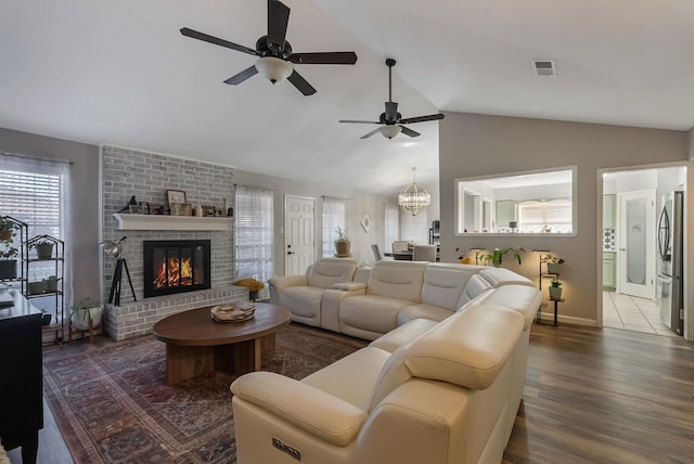 living room with a fireplace, vaulted ceiling, dark hardwood / wood-style flooring, and ceiling fan with notable chandelier