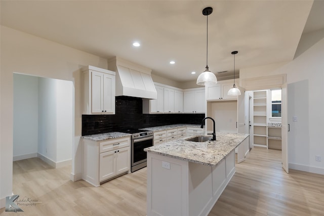 kitchen with sink, white cabinetry, stainless steel range with electric stovetop, light stone countertops, and a kitchen island with sink