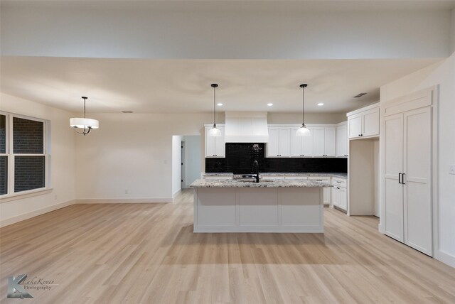 kitchen featuring light stone countertops, decorative light fixtures, white cabinets, and a kitchen island with sink