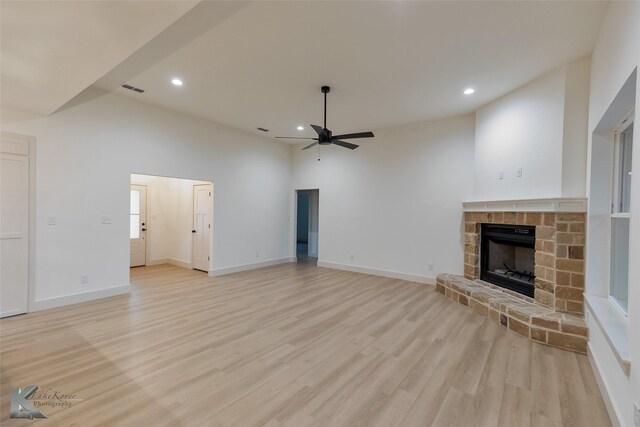 unfurnished living room featuring ceiling fan, a high ceiling, light wood-type flooring, and a stone fireplace