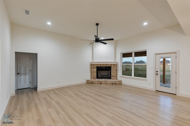 unfurnished living room featuring ceiling fan, visible vents, a fireplace with raised hearth, and light wood-style flooring