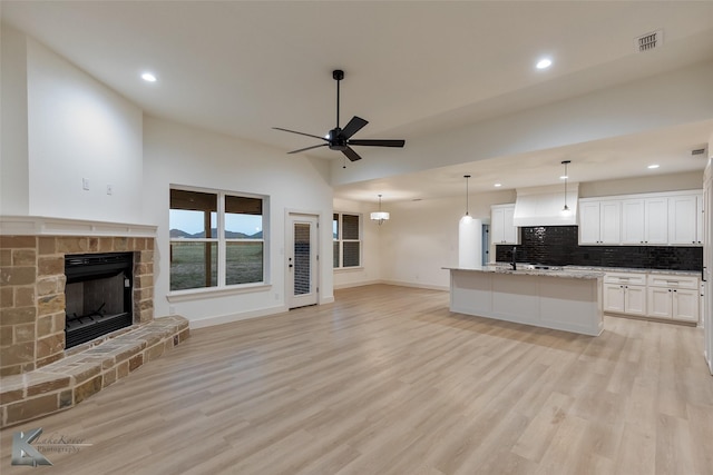 unfurnished living room with a stone fireplace, ceiling fan, light wood-type flooring, lofted ceiling, and sink