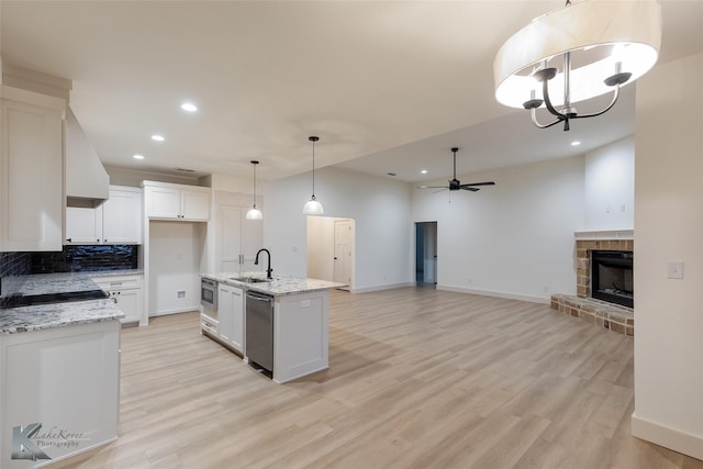 kitchen with light wood-style flooring, stainless steel appliances, a sink, white cabinets, and a brick fireplace