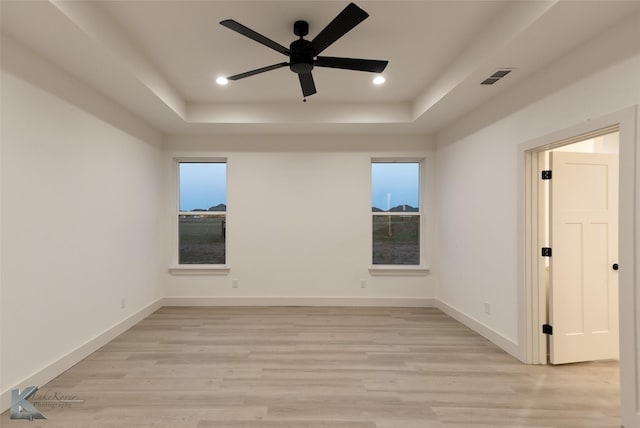 spare room with baseboards, visible vents, light wood-style flooring, ceiling fan, and a tray ceiling