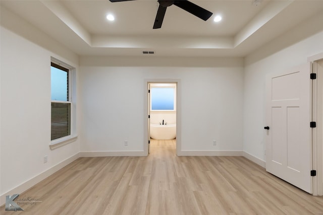 unfurnished room with a wealth of natural light, a tray ceiling, and light wood-type flooring