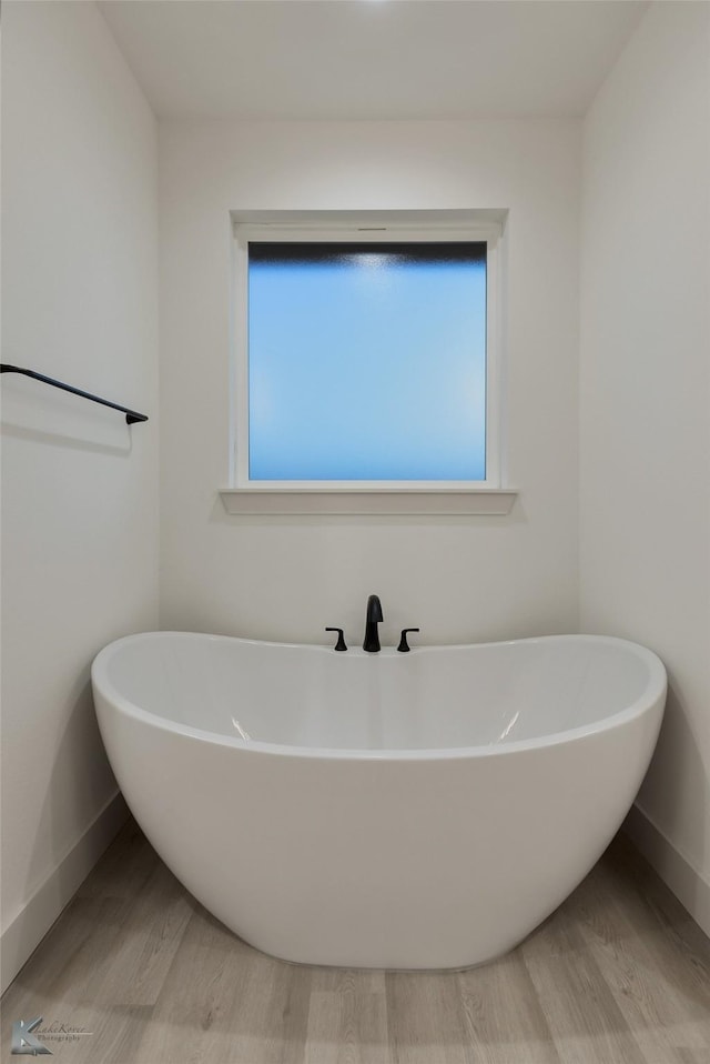 full bath with a freestanding tub, baseboards, and wood finished floors