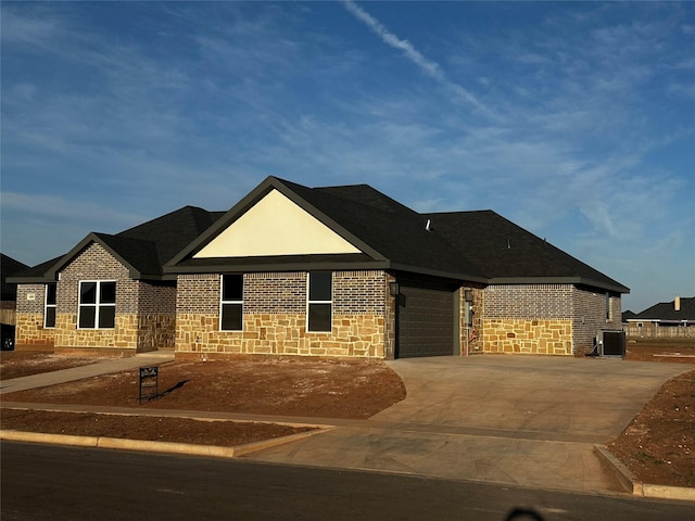 single story home with stone siding, concrete driveway, central AC, and an attached garage