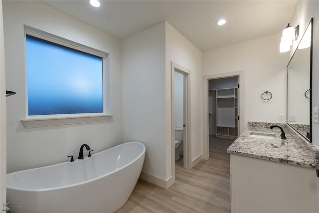 bathroom with baseboards, toilet, wood finished floors, a freestanding bath, and vanity