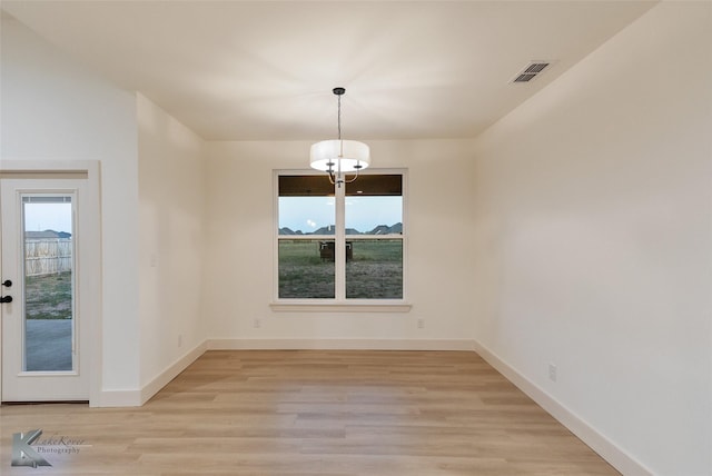 unfurnished dining area featuring baseboards, a notable chandelier, visible vents, and light wood-style floors