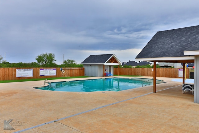 community pool with a patio, an outdoor structure, and fence