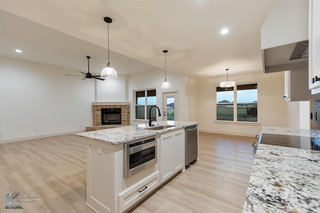 kitchen featuring a fireplace with raised hearth, a sink, white cabinetry, dishwasher, and wall chimney exhaust hood