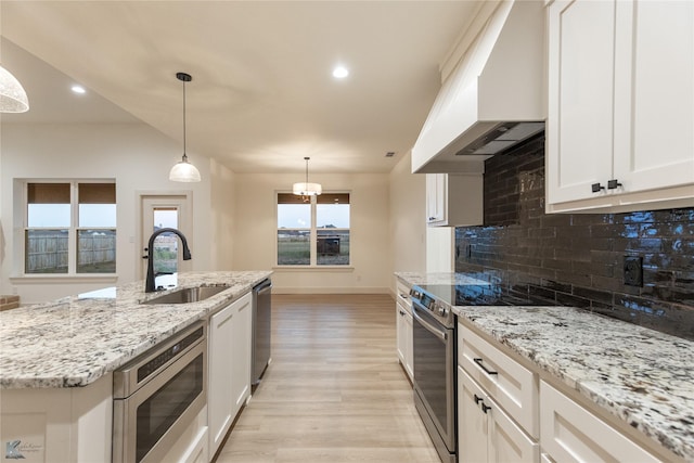 kitchen with custom exhaust hood, an island with sink, appliances with stainless steel finishes, decorative light fixtures, and sink