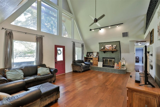 living room with ceiling fan, a fireplace, hardwood / wood-style floors, a high ceiling, and rail lighting