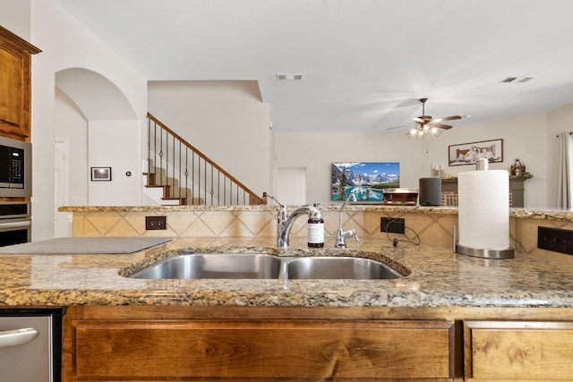 kitchen featuring stainless steel microwave, ceiling fan, light stone countertops, and sink