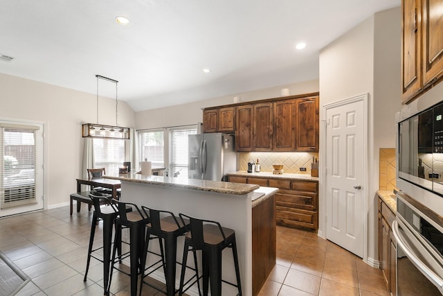 kitchen with pendant lighting, a center island, decorative backsplash, appliances with stainless steel finishes, and light tile patterned floors