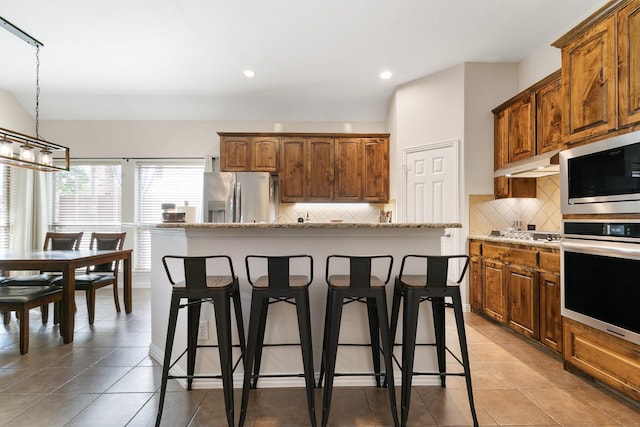 kitchen featuring pendant lighting, a kitchen island, stainless steel appliances, decorative backsplash, and light stone counters